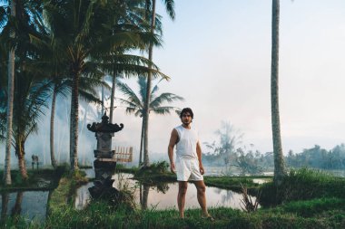 Ciddi sakallı, sıradan kıyafetli, çimenli çimlerde dikilip tropikal tatil beldesinde vakit geçirirken kameraya bakan bir grup ciddi etnik erkek gezgin.