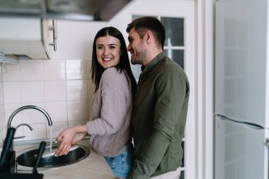 Mutfakta lavaboda musluk suyuyla temizlik yapmakla meşgulken kameraya gülümseyen genç bir erkeğin yan görüntüsü.