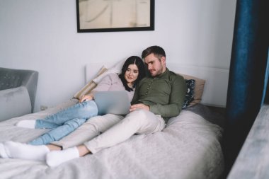 Rahat giysiler içinde, yumuşak yatakta yatıp rahat yatak odasında dizüstü bilgisayardan ilginç bir film izleyen pozitif erkek ve kadından oluşan bir vücut.