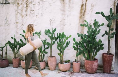 Çıplak ayaklı, çıplak ayaklı, elinde yuvarlak beyaz bir yastıkla gezen, otelin duvarları boyunca çömlek içindeki tropikal yeşil bitkilerin yanında yürüyen ve gözlerini kaçıran bir kadın.