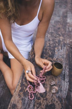 Yukarıdan gelen isimsiz bir kadın, tahta masada bacağı katlanmış bir şekilde oturuyor bir fincan kahveyle ve gün ışığında iki eliyle tespih çekiyor.