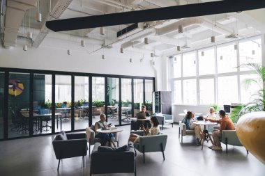 İş adamları birbirleriyle konuşuyor, aletlerle sörf yapıyor ve modern ofiste masalarda birlikte oturuyor ve başlangıç projesi üzerinde çalışıyorlar.