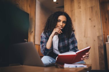 Masada dizüstü bilgisayarı olan genç bir kız öğrenci. Not defterindeki notları okuyup dudaklarına kalem tutarak kameraya bakıyor.