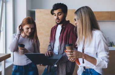 Bilgisayarlı, çok ırklı çalışanlardan oluşan bir ekip gündelik kıyafet içinde fikirleri paylaşıyor ve ofis mutfağında kahve içerken proje üzerinde işbirliği yapıyor.