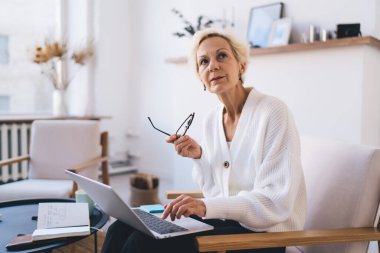 Ciddi kadın gözlük takıyor ve uzaktan iş projesinde çalışırken gözlerini kaçırıyor. Evdeki dinlenme odasındaki bilgisayarı kullanıyor.