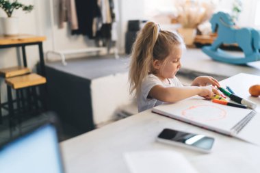At kuyruklu çocuk evde vakit geçirirken çizim defterinde çok renkli kalemlerle yaratıcılığını ifade ederek masada oturuyor.