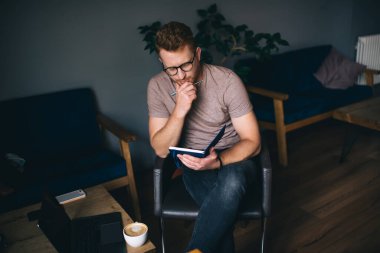 Kafeteryada bir fincan aromatik latte ve netbook ile vakit geçirirken elinde çene üzerine oturmuş, planlamacıda notlar yazan yüksek açılı bir adam.