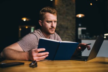 Modern dizüstü bilgisayarla internet sayfasında not defteri okuyarak bilgi veren Kafkasyalı ciddi blogcu, yetenekli öğrenci ve dijital netbook teknolojisi üzerine eğitim uygulaması yoluyla öğrenme