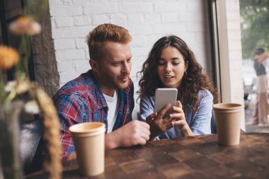 Kafkasyalı çift sosyal medya ağlarında web sayfası için içerik planını tartışırken birlikte cep telefonu teknolojisi kullanıyorlar. Milenyum hipster erkekleri kahve dükkanında cep telefonlarını tarıyorlar.