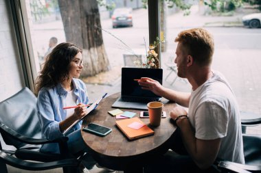 Erkeklerin dizüstü bilgisayarlı ekranı kadın meslektaşlarına gösterirken, birbirlerine bakarken, kahve fincanı ve kafede not defteriyle masada otururken, projeyi açıklarken yan görünümü