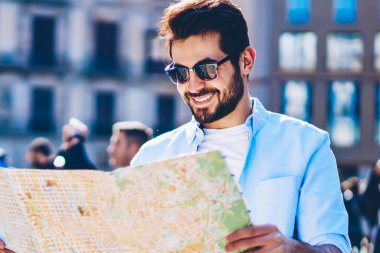 Mutlu sakallı rahat giyinmiş turizm yaz tatili sırasında güneşli günde mimari merkezi hedef ayakta aramak için adam okuma ve macera seyahat zevk şık güneş gözlüğü