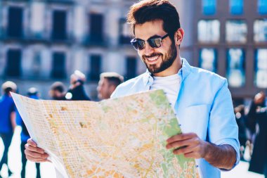 Mutlu sakallı rahat giyinmiş turizm yaz tatili sırasında güneşli günde mimari merkezi hedef ayakta aramak için adam okuma ve macera seyahat zevk şık güneş gözlüğü