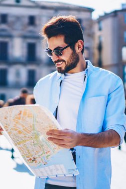 Doğru yol ve yön ayakta mimari kent merkezinde aramak için olumlu genç adam harita elinde tutan güneş gözlüğü. Mutlu erkek sevgilisi showplace yer için arayan seyahat