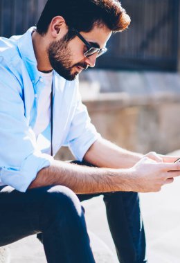 Siyah güneş gözlüklü şık genç adam, ücretsiz 4 internete bağlı modern akıllı telefondan sohbet ediyor. Gündelik kıyafet giymiş hippi adam sokakta telefonda ağlarda medyayı paylaşıyor.