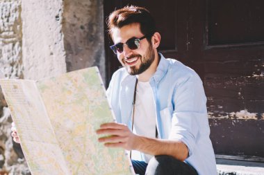 İlginç yerleri olan mutlu stil sahibi genç adam harita okuyor ve şehrin aşağısındaki mimari merdivenlerde otururken rotasını belirliyor. Olumlu sakallı turistler tatil beldelerini arıyor.