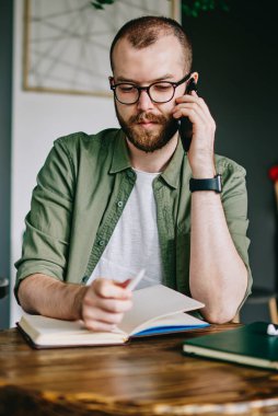Düşünceli hipster adam sakallı oturma favori kafeterya, erkek öğrenci tarafından ders kitabı içinde café okuma ve düzeltme notu Üniversitesi kampüsünde eğitim ve planları hakkında düşünme gözlük