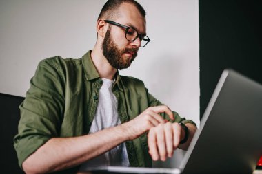 Yakışıklı delikanlı laptop en sevdiğim kafede, Erkek masada oturan ve bekleyen son gadget'ı organize ederken bilgisayarla çalışma fotoğraf yolu ile sohbet ederken onun smartwatch zamanında kontrol