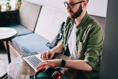 Çatı katı iç ve uzaktan çalışma ile kafede oturan gözlük ciddi yetenekli beyaz programcı, genç düşünceli laptop ve fikirler için kurs metin yazarak izlerken webinar adam.