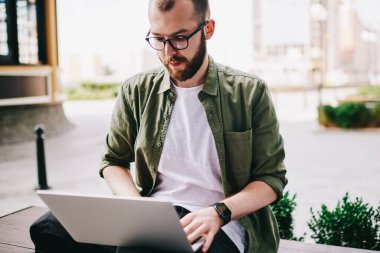 Dizüstü bilgisayar ile bankta oturmuş ve yeni modern elektronik aygıt için Gözat Web sitesi kullanarak proje hazırlama webinar online, profesyonel programcı izlerken kendinden emin ve düşünceli genç adam