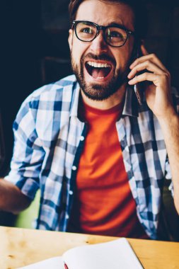 Kızgın sakallı hippi biri üstten görünüm alanı coworking çalışma dijital Smartphone cep telefonu ile telefon görüşmesi sırasında rahat kıyafet bağırarak giymiş. Ağlama ve hareket eden telefon aygıt üzerinde savunarak öfkeli genç adam