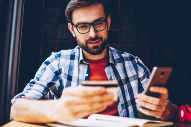 Dalgın casual giyinen hipster adam web sitesinde sipariş yapmak için kartvizit smartphone telefon numarasını çevirme. Yapım para hareket online üstünde hareket eden telefon içinde coworking oturan genç adam
