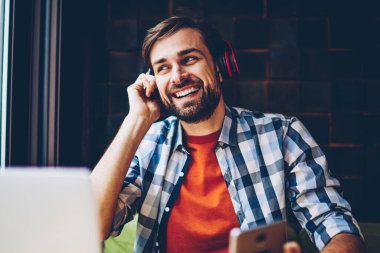 Telefon için Bluetooth kulaklık elektronik müzik zevk olumlu sakallı blogger bağlı. Neşeli rahat giyinmiş genç adam dinleme ses şarkı çalma listesinden Smartphone'da indirilen