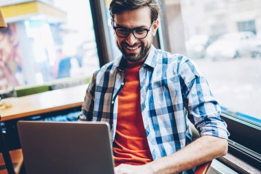 Gülüyor ve laptop sosyal ağlarda arkadaşlarınızla çevrimiçi sohbet neşeli sakallı hippi adamın bağlantısı için 4 g kablosuz internet. Komik Haberler Netbook coworking içinde okuma olumlu erkek blogger