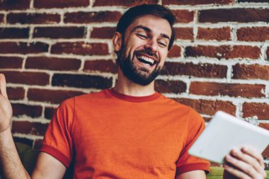 Gülen ve izleyerek yaşamak akarsu online 4 g internet bağlantısı ile modern tablet neşeli genç adam. Pozitif sakallı hippi adam dijital dokunmatik ped cihaz coworking içinde oturan iyi haberleri okuyun