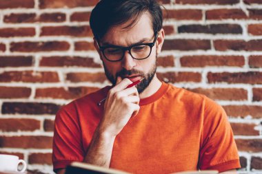 Dalgın akıllı öğrenci ders kitabı okuyan görev okuma ve çözüm üzerinde düşünme sakallı. Kitap yaklaşan sınavlar için hazırlama bilgilerinden öğrenme gözlük düşünceli akıllı genç adam