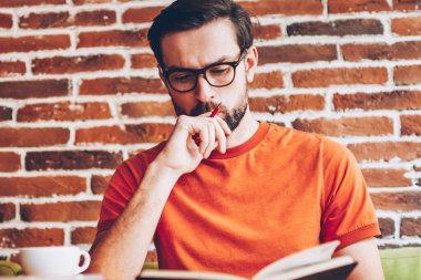 Akıllı hipster öğrenci ders kitabı hazırlama semineri için bilgilerin öğrenme konsantre. Coworking modern netbook ile masada oturan görev çalışmaya düşünme dalgın genç adam