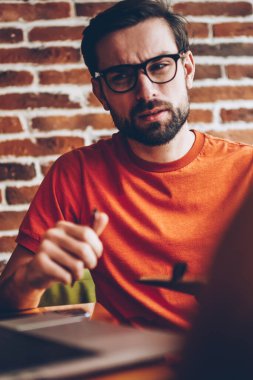 Şüpheci sakallı genç adam optik gözlük için 4 g bağlı modern dizüstü bilgisayar aygıt bakarak internet ve teknik sorun alanı iç coworking oturan düşünme