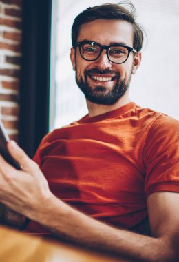Gözlük vizyon düzeltme kafede oturan 4 g internet bağlantısı ile modern smartphone uygulama yüklenirken kameraya gülümseyen pozitif sakallı genç adam portresi yarım uzunluk