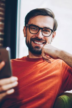 Başarılı sakallı erkek blogger smartphone aygıt ücretsiz 4 g internet bağlantısı üzerinden app karşıdan yüklerken kameraya gülme portresi. Pozitif hipster adam cep üzerinde online ödeme yapma