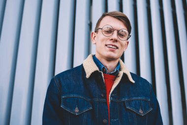 Neşeli genç öğrencinin yarım uzunluk portre kameraya gülme şık denim giyim giymiş. Kentsel ortamda poz vizyon düzeltme optik gözlük olumlu hipster adam
