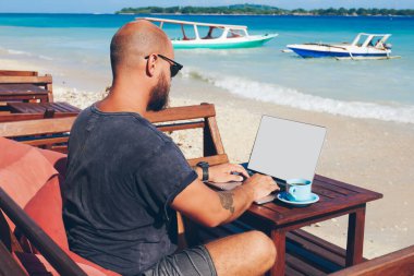 Online onun iş dizüstü bilgisayar üzerinden çalışırken okyanus kıyısında dinlenme, bin yıllık hipster adam güncelleştirme içeriği gezi hakkında yayın klavye içinde onun blogg yetenekli erkek serbest meslek