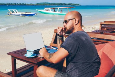 Düşünceli erkek serbest yazar, okyanus kıyısında dizüstü bilgisayarla yeniden oluşturulan yeni bir makale hakkında düşünüyor, iş adamı tatilde uzaktan kumandalı iş için netbook kullanıyor.