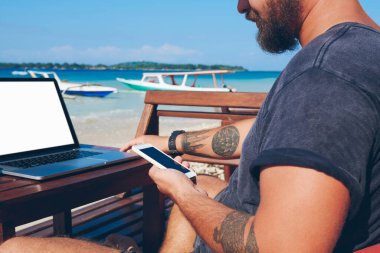 Cep telefonunu elinde tutan, bankacılık dengesini kontrol eden, okyanus sahilinde işlem yapan, uzaktan kumanda sırasında teknolojiyi kullanan bir adamın görüntüsü. Cep telefonu ve netbook 'u senkronize et.