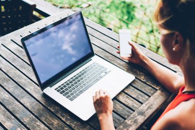 Multimedya dosyalarını netbook ile senkronize ederken, cep telefonu tutan bin yıllık kadının arka planı, terasta masada oturan serbest çalışan kadın bilgisayarla uzaktan kumanda için boş ekran kullanan