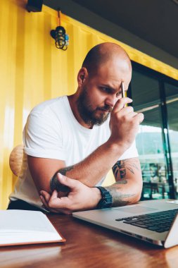 Konsantre erkek öğrenci sorun izlerken online eğitim kursları dizüstü bilgisayar, netbook, bilgi okuma projesi hakkında düşünme yetenekli erkek Tasarımcısı üzerinden sırasında çözme şaşkın