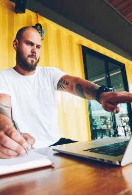 Akıllı beyaz erkek öğrenci üniversite kampüsünde, bin yıllık adam netbook monitörde işaret ve notlar dizüstü bilgisayar kullanan ödev not defterine web sayfasından bilgi kopyalama