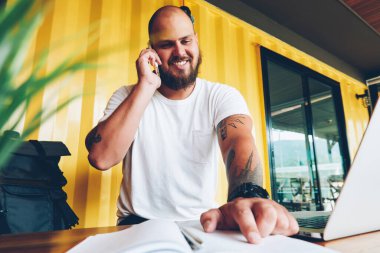 Not defteri paylaşım bilgileri cep telefonu konuşma sırasında notlarda işaret eden neşeli hipster adam. mutlu erkek öğrenci üniversite kampüsünün dizüstü bilgisayar ile oturup ödev hakkında danışmanlık arkadaş arama