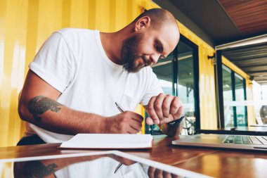 Notlar ve kol saati çalışma günü planlama ve fikirleri not defterinde yazılı zaman bakarak ciddi genç adam bu iş için dizüstü bilgisayarın yakınında oturan zamanında yönetme düşünceli erkek serbest meslek