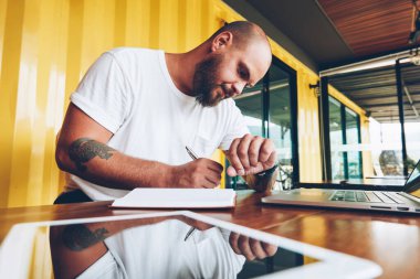 Notlar ve kol saati çalışma günü planlama ve fikirleri not defterinde yazılı zaman bakarak ciddi genç adam bu iş için dizüstü bilgisayarın yakınında oturan zamanında yönetme düşünceli erkek serbest meslek