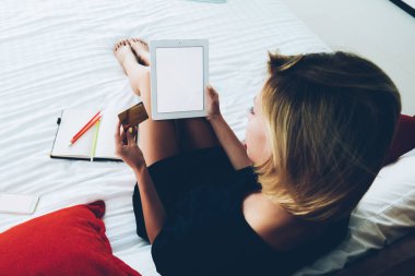 Genç bir kadının portatif bilgisayar uygulaması üzerinden kredi kartı kullanarak alışveriş yapmasının en üst görüntüsü, hippi kız tablet aracılığıyla web mağazasından alışveriş yapıyor ve web sayfasında yatmakta olan eşyalar için ödeme yapıyor.