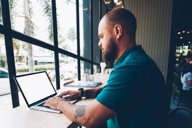 Ciddi sakallı bir erkek blogcu dizüstü bilgisayarında sosyal ağlarda ekran sohbetlerini taklit ederek mesaj yazıyor. İnternet üzerinden e-postaları kontrol eden kalem adam kafenin iç kısımlarında serbest çalışmalar yapıyor.