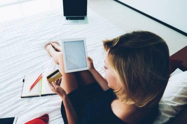 Yatağın üzerinde otururken kredi kartı numarasını kullanan genç hippi kız, taşınabilir bilgisayarla online alışveriş yapıyor rahat bir evde boş zaman geçiriyor.