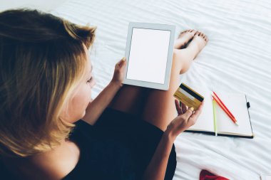 Taşınabilir bilgisayarla para kazanan bir kadının evdeki rahat yatağında oturması, hister kızın internet mağazasında dijital tablet kullanarak alışveriş yapması ve internet bankacılığı yapması.