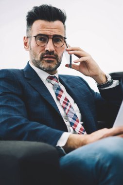 Olgun işadamı portresi Smartphone'da office belgelerinde denetleme sırasında iletişim sırasında kameraya bakarak formal giyim giymiş. Elinde cep üzerinde arama raporları ile gurur ceo