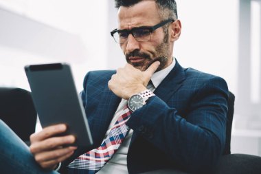 Konsantre orta yaşlı tüccar web sitesinde ücretsiz 4 g internet bağlantısı ile modern dokunmatik yüzey üzerinde dikkatle finansal haber okuma formal giyim. Dalgın olgun gurur CEO'su tablet video izlerken