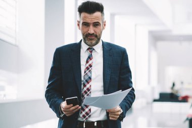 Orta yaşlı başarılı gurur CEO'su portresi finansal belgeler elinde tutarken kameraya gülümseyen formal giyim giymiş. Smartphone ayakta Office ile müreffeh icra müdürü